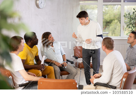 Guy talking to male colleagues gathered in office lounge room 103588510