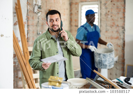 Engineer holds an estimate in his hands, talking on a mobile phone 103588517
