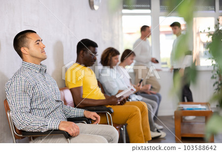 Young male visitor sitting on the bench in waiting room of clinic Young male visitor sitting on the bench in waiting room of clinic 103588642