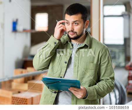Focused man standing at indoors building site, reading document Focused man standing at indoors building site, reading document 103588659