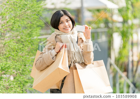 A young woman wearing a beige coat and holding many paper bags and a credit card shopping image A young woman wearing a beige coat and holding many paper bags and a credit card shopping image 103589908