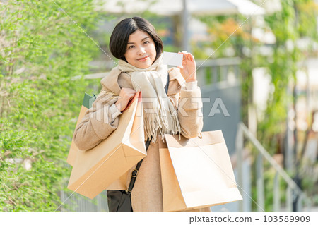 一位身穿米色外套、拿著許多紙袋和信用卡購物圖像的年輕女性 一位身穿米色外套、拿著許多紙袋和信用卡購物圖像的年輕女性 103589909
