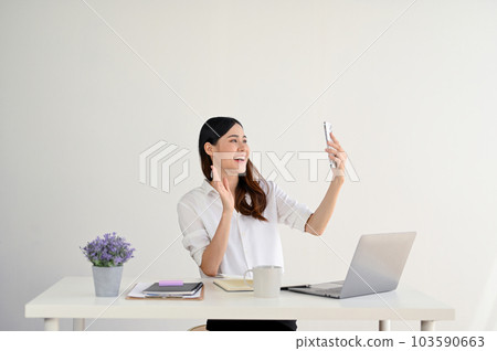 A cheerful Asian businesswoman is talking with her friends through a video call on her smartphone 103590663