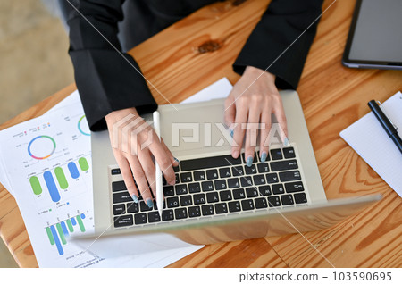 Top view of a businesswoman using her laptop and analyzing financial data at her desk. Top view of a businesswoman using her laptop and analyzing financial data at her desk. 103590695