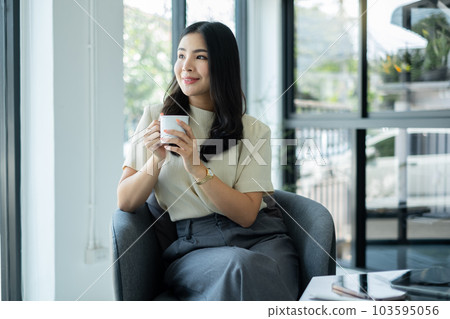 Asian businesswoman smiling happily with a new morning holding a cup of coffee lightly sipping coffee professional woman in size working in the office 103595056