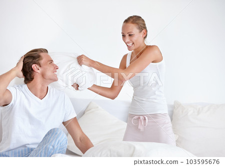 Playful, energy and couple in a pillow fight on the bed in the hotel room on romantic weekend trip. Happiness, laughing and young woman and man playing together in the morning in the bedroom at home. Playful, energy and couple in a pillow fight on the bed in the hotel room on romantic weekend trip. Happiness, laughing and young woman and man playing together in the morning in the bedroom at home. 103595676