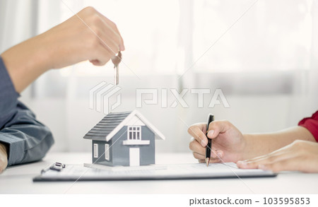 Real estate agent broker hand over the house key to the new owner after completing the signing according to agreement renting a house and buy house insurance Home insurance concept 103595853