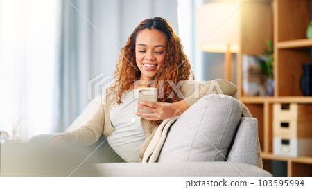 Young woman smiling and laughing while texting on a phone at home. Cheerful female chatting to her friends on social media, browsing online and watching funny internet memes while relaxing on a sofa 103595994