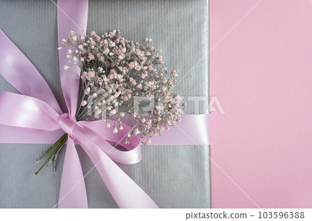 Gray gift box decorated with pink ribbon and small bouquet of gypsophila. 103596388