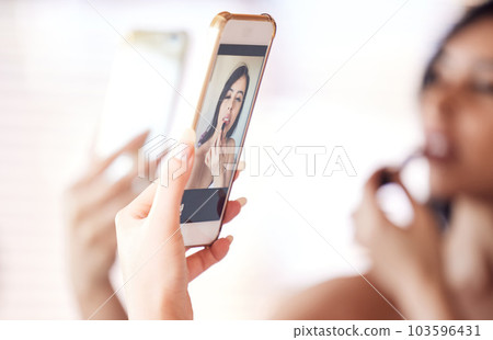 I love the way this camera makes me look. Shot of a beautiful young woman using her phone as a mirror while applying lipstick at home. 103596431