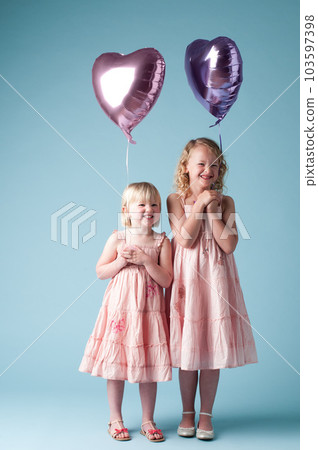 Were never giving these up. Shot of two little girls holding heart balloons against a studio background. Were never giving these up. Shot of two little girls holding heart balloons against a studio background. 103597398