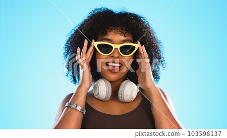 Trendy black woman face isolated on blue background for beauty, cosmetics and fashion of gen z lifestyle. Confident african american person or model with cool sunglasses and headphones for summer Trendy black woman face isolated on blue background for beauty, cosmetics and fashion of gen z lifestyle. Confident african american person or model with cool sunglasses and headphones for summer 103598137