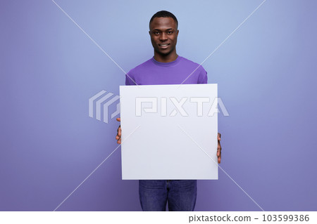 young attractive african man dressed in basic t-shirt holding a white poster mockup for advertising 103599386
