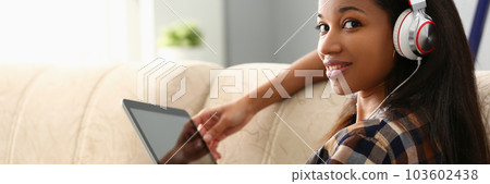 Young beautiful african american woman in headphones uses tablet Young beautiful african american woman in headphones uses tablet 103602438