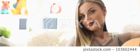 Beautiful young woman is sitting on sofa with guitar Beautiful young woman is sitting on sofa with guitar 103602444