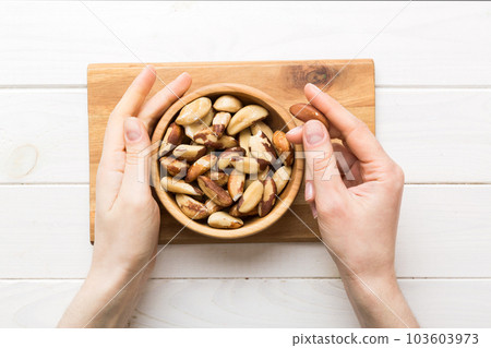 Woman hands holding a wooden bowl with brazil or bertholletia nuts. Healthy food and snack. Vegetarian snacks of different nuts 103603973