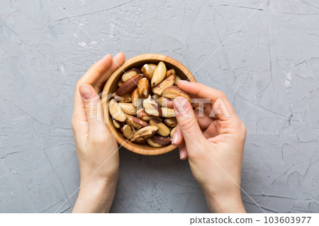 Woman hands holding a wooden bowl with brazil or bertholletia nuts. Healthy food and snack. Vegetarian snacks of different nuts Woman hands holding a wooden bowl with brazil or bertholletia nuts. Healthy food and snack. Vegetarian snacks of different nuts 103603977