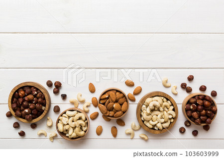 Assortment of nuts in wooden bowl on colored table. Cashew, hazelnuts, walnuts, almonds. Mix of nuts Top view with copy space Assortment of nuts in wooden bowl on colored table. Cashew, hazelnuts, walnuts, almonds. Mix of nuts Top view with copy space 103603999