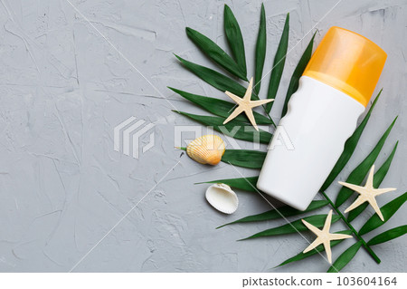 Sunscreen spray bottle. Bottle with sun protection cream and sea shells with tropical green leaf on color background, top view 103604164