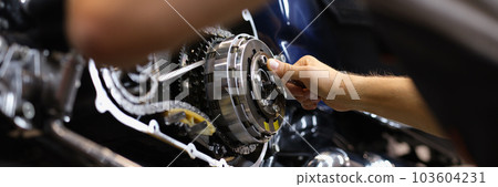 Mechanic repairs motor and chain of motorcycle in workshop 103604231