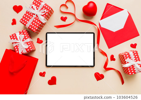 Top view of digital tablet with gift boxes and hearts on colorful background. Tablet with black screen with Holiday decorations gift box top view 103604526