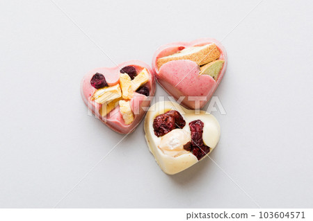 chocolate sweets in the form of a heart with fruits and nuts on a colored background. top view with space for text, holiday concept chocolate sweets in the form of a heart with fruits and nuts on a colored background. top view with space for text, holiday concept 103604571