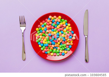 cutlery on table and sweet plate of candy. Health and obesity concept, top view on colored background cutlery on table and sweet plate of candy. Health and obesity concept, top view on colored background 103604585