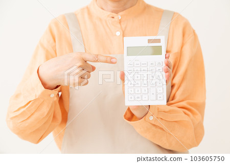 A senior female housewife in a casual appearance wearing an apron pointing at a calculator A senior female housewife in a casual appearance wearing an apron pointing at a calculator 103605750