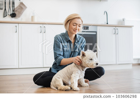 Female adult rubbing ears of terrier on kitchen floor Female adult rubbing ears of terrier on kitchen floor 103606298