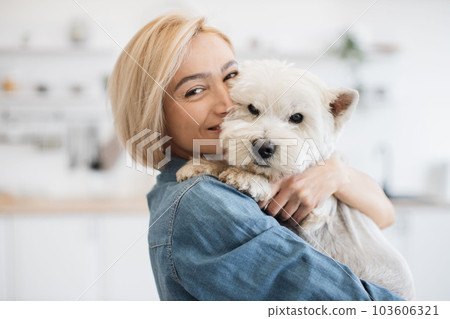 Female pet owner posing with terrier in arms in kitchen 103606321