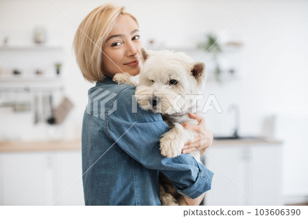 Female pet owner posing with terrier in arms in kitchen 103606390
