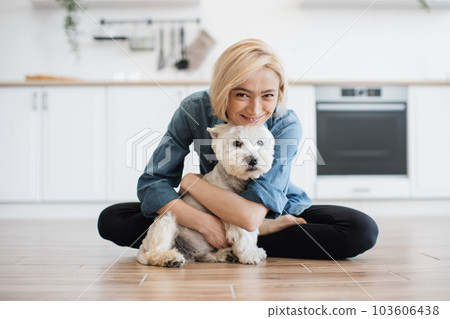 Woman hugging little dog while posing on floor in kitchen 103606438
