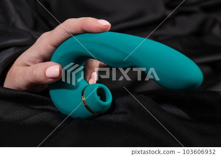 A woman is holding a green sex toy lying on a black silk sheet. 103606932