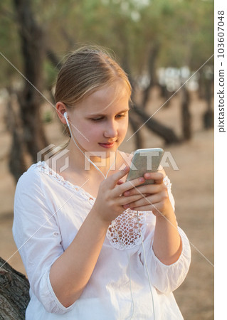 Teenage girl in headphones holding mobile phone on the background of forest 103607048