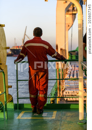 Seaman in red working overall and orange helmet on deck. Working at sea. Cargo vessel. Mooring operations. Able seaman. 103607345