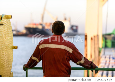 Seaman in red working overall and orange helmet on deck. Working at sea. Cargo vessel. Mooring operations. Able seaman. 103607346