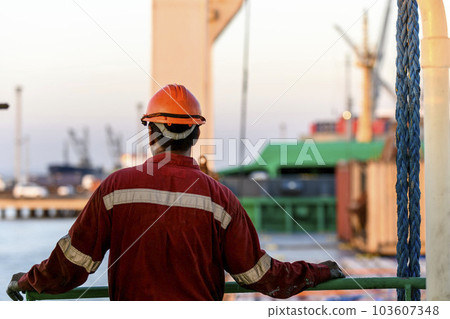 Seaman in red working overall and orange helmet on deck. Working at sea. Cargo vessel. Mooring operations. Able seaman. Seaman in red working overall and orange helmet on deck. Working at sea. Cargo vessel. Mooring operations. Able seaman. 103607348