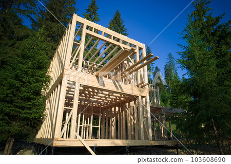 Drone's vantage point offers view of two-storey wooden-framed domicile in process of construction near forest. Idea of contemporary ecological construction and modern architectural design. 103608690