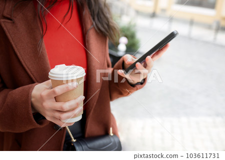 Woman uses smart phone on the street and sips coffee. Woman uses smart phone on the street and sips coffee. 103611731