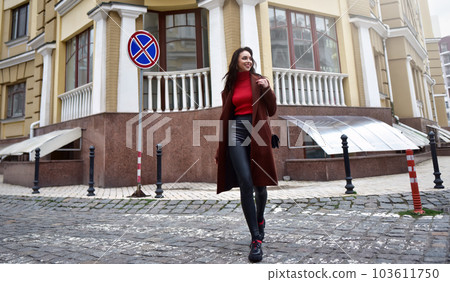 Beautiful woman with a purse on her shoulder in a brown coat is walking down the street. Beautiful woman with a purse on her shoulder in a brown coat is walking down the street. 103611750