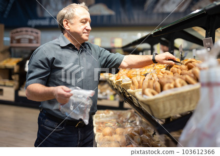 Elderly male shopper chooses hot fresh buns and bread in supermarket 103612366