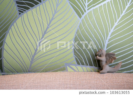 Unglazed earthenware dragon figurine in front of leafy wallpaper Unglazed earthenware dragon figurine in front of leafy wallpaper 103613055