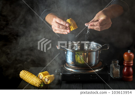 A professional chef adds salt to the pot when cooking corn. Work environment on a vintage kitchen table in a restaurant 103613954