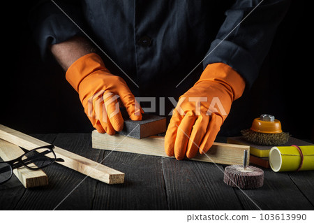 Woodworker cleans a wooden plank with an abrasive tool. Hands of the builder close-up during work. Renovation or construction idea Woodworker cleans a wooden plank with an abrasive tool. Hands of the builder close-up during work. Renovation or construction idea 103613990