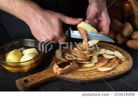 Professional chef peels potatoes for French fries. For potato dishes. On black background concept for menu, cooking, healthy food. Free advertising space Professional chef peels potatoes for French fries. For potato dishes. On black background concept for menu, cooking, healthy food. Free advertising space 103614006