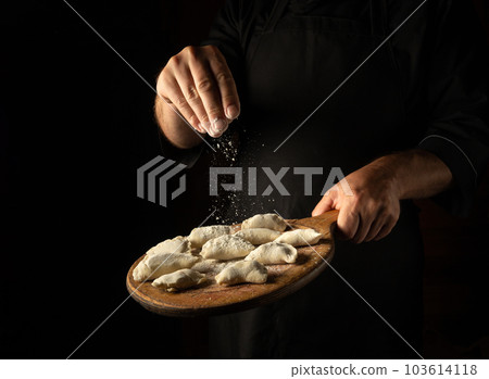 The chef throws flour on meat dumplings on a cutting board. Concept for a hotel menu on a black background with space for advertising. 103614118
