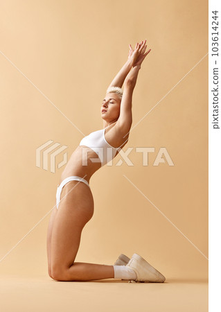 Portrait of sportive young woman with slim, fit body posing in cotton underwear against pastel yellow studio background 103614244