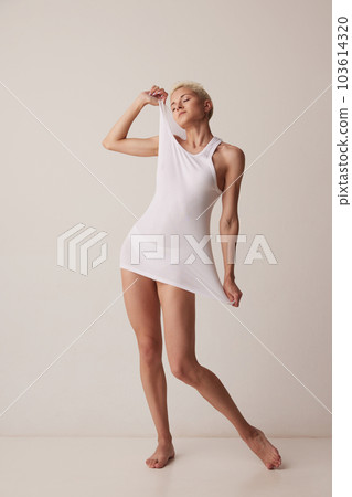 Full-length portrait of slim, beautiful young woman posing in white singlet, homewear against grey studio background Full-length portrait of slim, beautiful young woman posing in white singlet, homewear against grey studio background 103614320