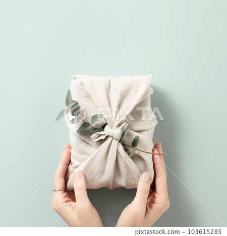 Female hands holding a gift in eco friendly reusable fabric package on blue background 103615285