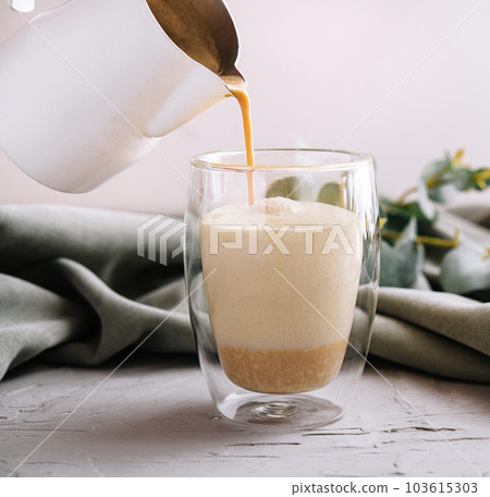 pouring a coffee with milk from teapot to glass cup 103615303